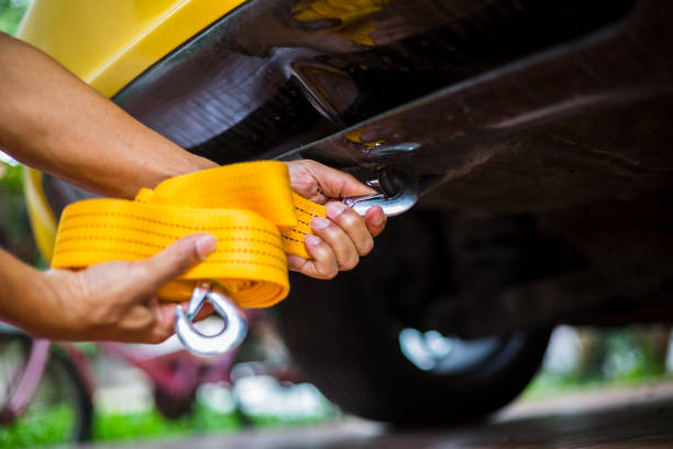 mains de l'homme retenant la courroie jaune de remorquage de voiture avec la voiture jaune. - crochet équipement photos et images de collection