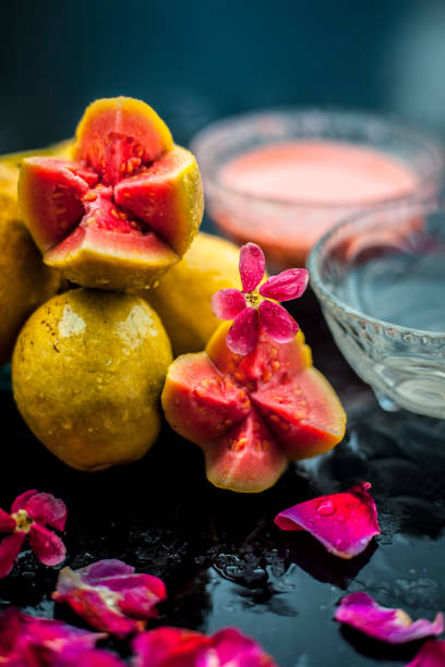 Guava pulp and water well mixed in a glass bowl on the wooden surface along with some raw cut guava, with some rose petals, also completing a face mask used for a natural glow. Guava pulp and water well mixed in a glass bowl on the wooden surface along with some raw cut guava, with some rose petals, also completing a face mask used for a natural glow. guava photos stock pictures, royalty-free photos & images