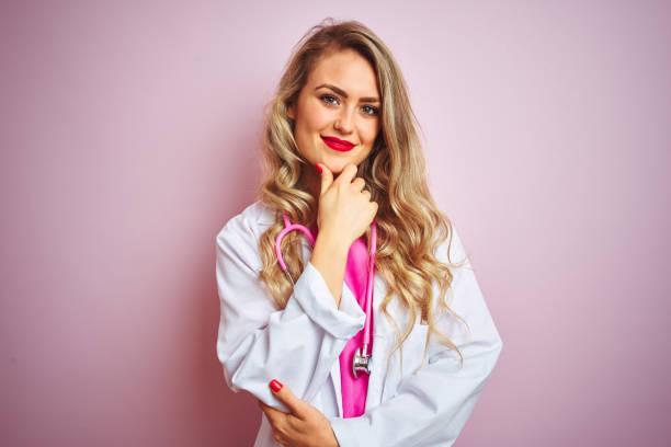 istock Young beautiful doctor woman using stethoscope over pink isolated background looking confident at the camera smiling with crossed arms and hand raised on chin. Thinking positive. 1173835670