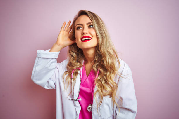 istock Young beautiful doctor woman using stethoscope over pink isolated background smiling with hand over ear listening an hearing to rumor or gossip. Deafness concept. 1173835722