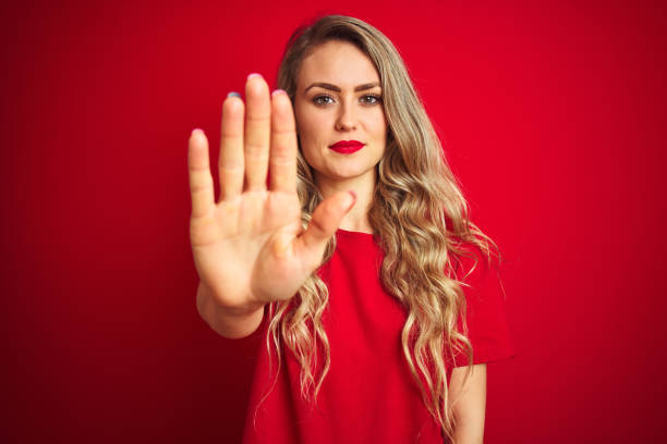 istock Young beautiful woman wearing basic t-shirt standing over red isolated background doing stop sing with palm of the hand. Warning expression with negative and serious gesture on the face. 1173838347