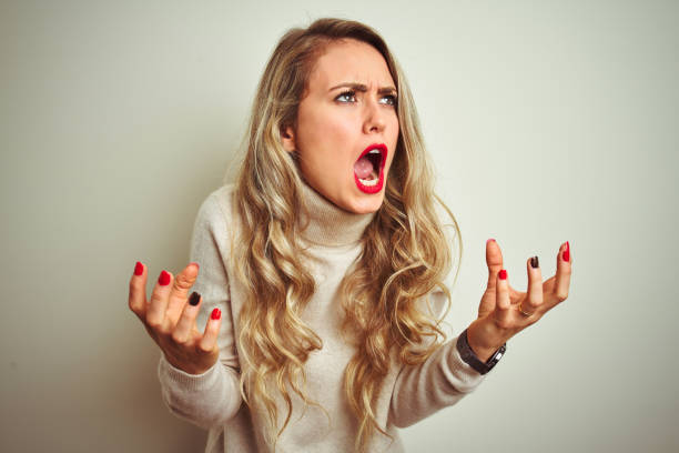 belle femme utilisant le chandail de col roulé d'hiver au-dessus du fond blanc isolé fou et fou criant et criant avec l'expression agressive et les bras soulevés. concept de frustration. - blond hair photos et images de collection