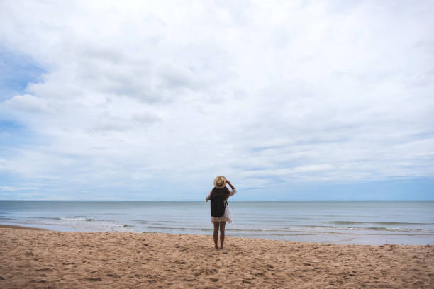 istock A female traveler with hat and backpack standing alone on the beach 1173843482