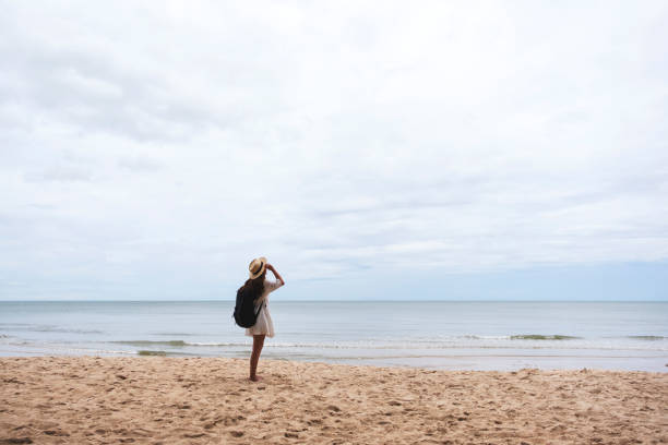 istock A female traveler with hat and backpack standing alone on the beach 1173843581