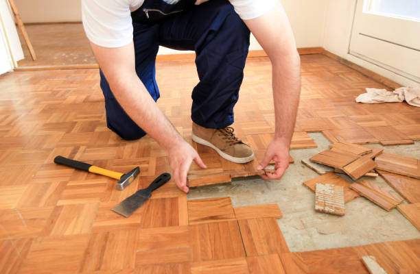 Construction worker and constructor is working on renovation of apartment. Handyman is removing old wooden parquet flooring using yellow hammer and scraping tool. Builder dismantles parquet floor.