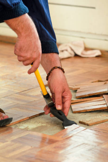 istock Construction worker and constructor is working on renovation of apartment. Handyman is removing old wooden parquet flooring using yellow hammer and scraping tool. Builder dismantles parquet floor. 1173844179