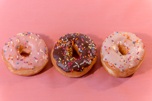 Trio of yummy iced donuts with sprinkles on a pink background