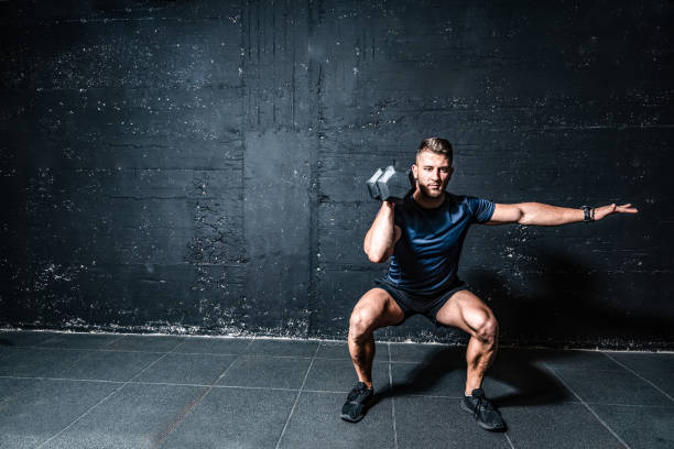 jeune homme en sueur musculaire fort de forme avec de grands muscles force croix d'entraînement de formation avec des poids d'haltères dans l'image foncée de gymnastique avec des personnes réelles d'ombres - human muscle muscular build dumbbell sports training photos et images de collection