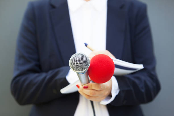 istock Female journalist at news conference, writing notes, holding microphone 1173853114