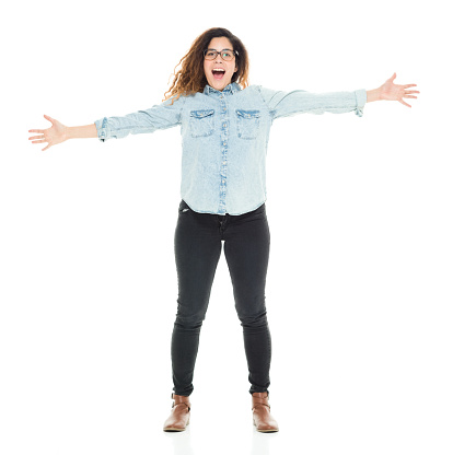 Full length / front view / looking at camera of 30-39 years old adult beautiful curly hair / long hair puerto rican ethnicity / latin american and hispanic ethnicity female / young women standing in front of white background wearing eyeglasses / button down shirt / shirt / jeans / pants who is smiling / happy / cheerful / cool attitude and showing arms outstretched / hand raised with arms raised