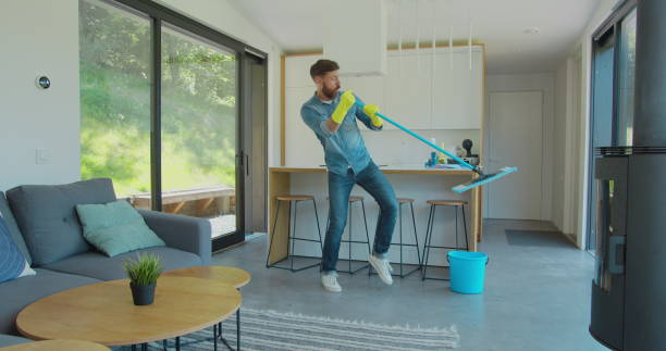 istock Man in protective gloves is singing using a mop and dancing while cleaning his house in living room during end of year clean. 1173877553