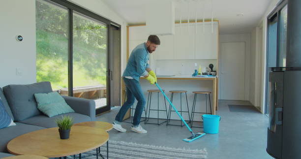 istock Man in protective gloves is singing using a mop and dancing while cleaning his house in living room during end of year clean. 1173877569
