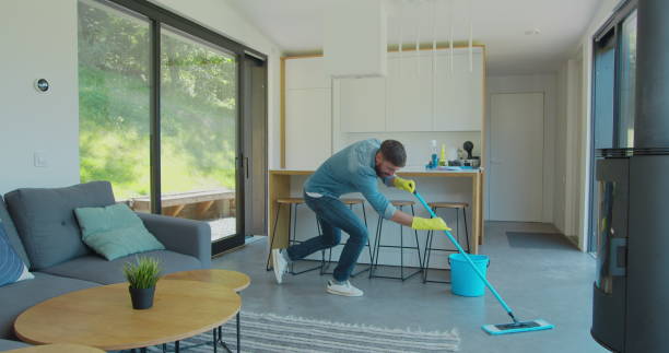 istock Man in protective gloves is singing using a mop and dancing while cleaning his house in living room during end of year clean. 1173877588