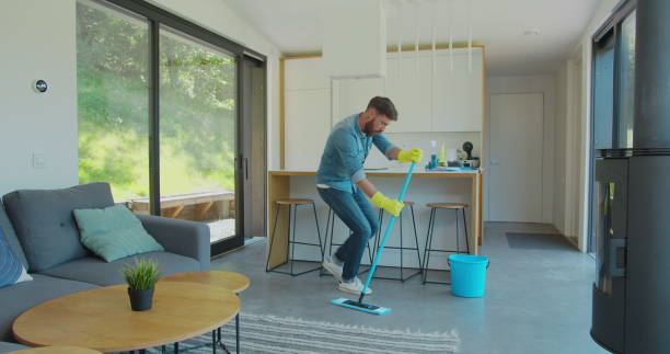 istock Man in protective gloves is singing using a mop and dancing while cleaning his house in living room during end of year clean. 1173877613