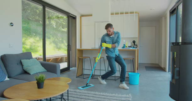 istock Man in protective gloves is singing using a mop and dancing while cleaning his house in living room during end of year clean. 1173877640
