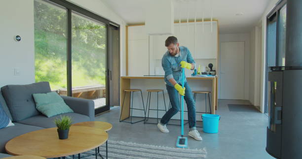 istock Man in protective gloves is singing using a mop and dancing while cleaning his house in living room during end of year clean. 1173877668