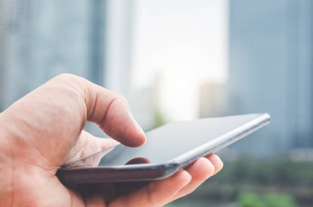 istock close up handsome man using hand typing smartphones and touch screen working search with app devices outdoor in city with sunrise and building background. 5G technology connecting the world. 1173877829