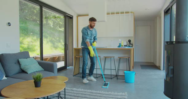 istock Man in protective gloves is singing using a mop and dancing while cleaning his house in living room during end of year clean. 1173877841