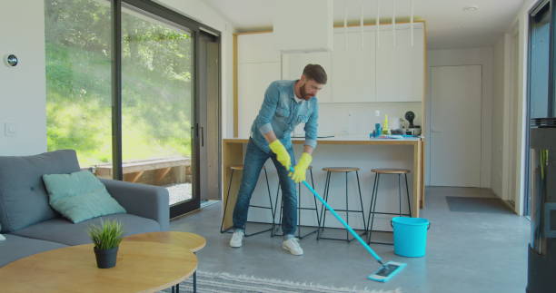 istock Man in protective gloves is singing using a mop and dancing while cleaning his house in living room during end of year clean. 1173877865