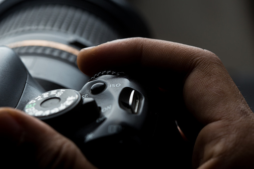 man's hand holding a DSLR camera in dim lighting