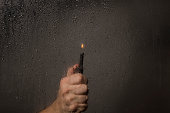Man hand holding burning lighter next to a wet window.
