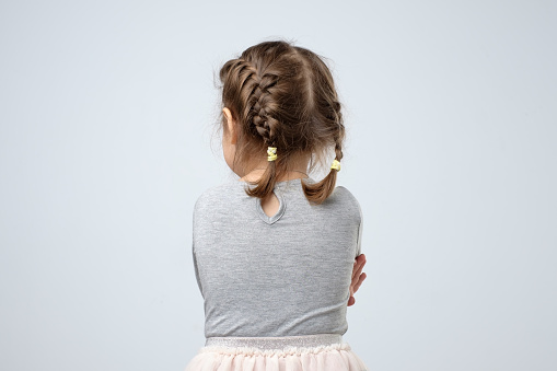 Rear view of little caucasian girl. Kid is lost or being offended on her parents. Studio shot