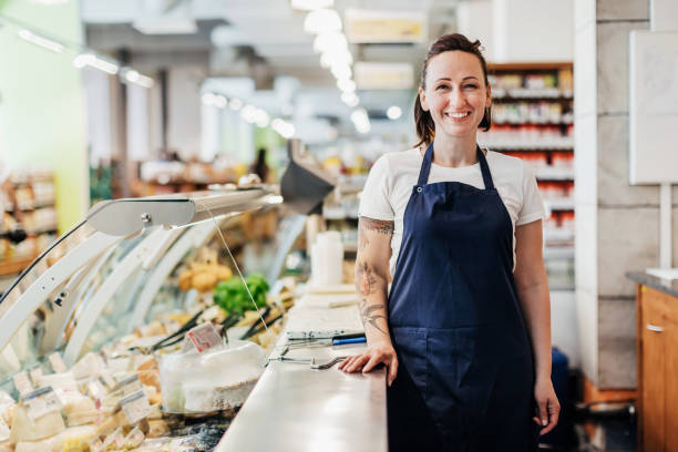 Portrait Of Supermarket Clerk Standing At Counter A portrait of a supermarket clerk smiling, wearing overalls while at work. delicatessen stock pictures, royalty-free photos & images