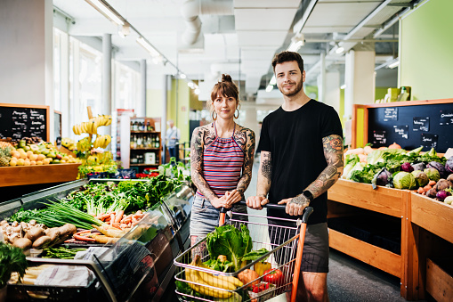A portrait of a young hipster couple with tattoos out shopping for groceries together at their local supermarket.