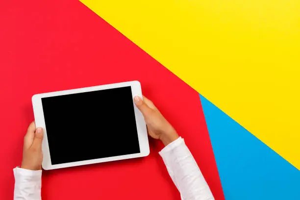 Photo of Kid hands with tablet computer on red, yellow and blue background