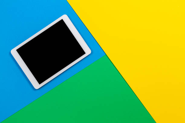 istock Digital tablet computer on light blue, green and yellow background. Top view 1173897148