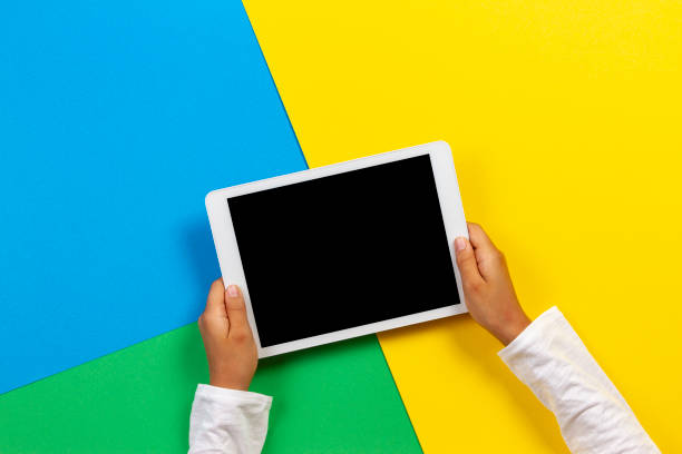 istock Kid hands with tablet computer on yellow, blue and green background 1173897171
