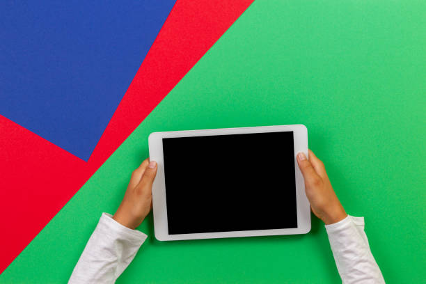 istock Kid hands holding white tablet computer on light green, blue and red background 1173897348