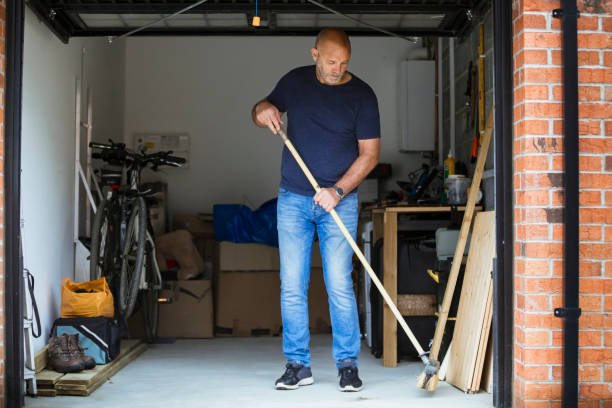 Sweeping His Garage Floor A man is sweeping the floor up his home garage with a large brush. The garage door is open. garage door opener photos stock pictures, royalty-free photos & images
