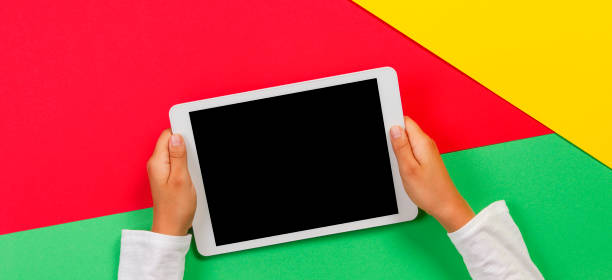 istock Kid hands with tablet computer on red, yellow and green background 1173897408