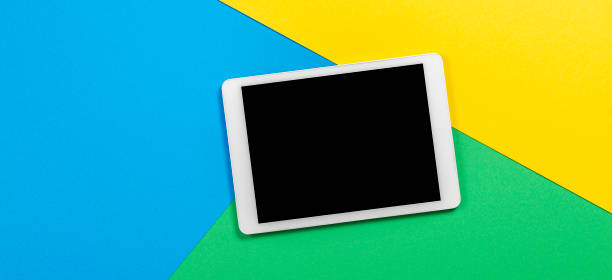istock Digital tablet computer on light blue, green and yellow background. Top view 1173897629