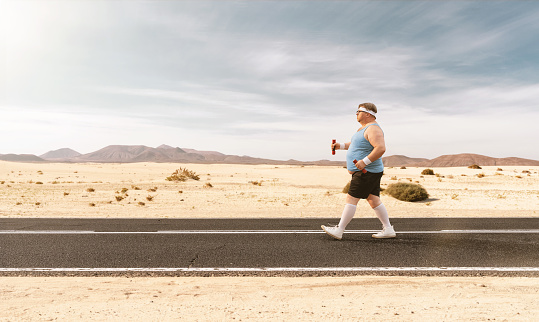 Funny overweight man jogging on the empty road with copy space