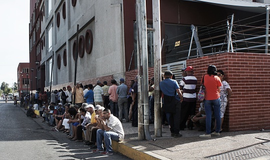 People standing up and sitting in sidewalk waiting patiently to buy supplies from food store