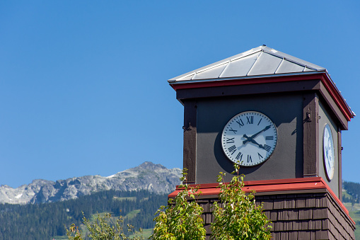 Roman Numeral Clock Tower with rocky mountains and blue sky in the background.