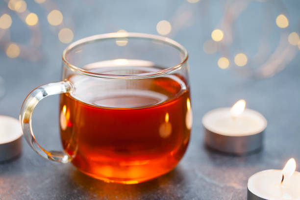 istock Black tea in glass cup with candles and light garland. Grey background. Copy space. 1173921589