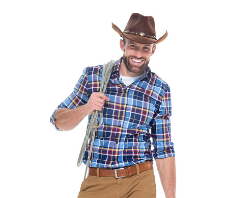 One man only / waist up / front view / looking at camera of 30-39 years old adult handsome people brown hair / with beard / short hair caucasian male / young men cowboy standing in front of white background wearing button down shirt / shirt / gingham / khaki pants / cowboy hat / hat who is smiling / happy / cheerful / cool attitude and holding lasso / using rope
