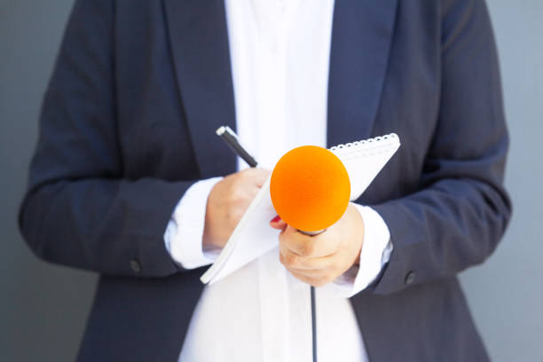 istock Female reporter at press conference or media event, writing notes, holding microphone 1173929985