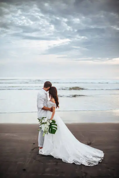Photo of Elegant gorgeous bride and groom walking on ocean beach during sunset time.