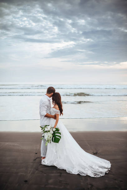 elegancka wspaniała narzeczeni spacerujący po plaży nad oceanem w czasie zachodu słońca. - wedding beach bride groom zdjęcia i obrazy z banku zdjęć