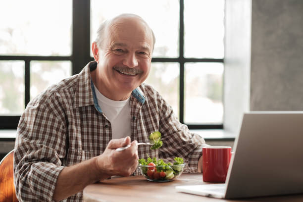 przystojny uśmiechnięty dojrzały mężczyzna o zdrowym śniadaniu siedząc w kuchni - retirement senior adult breakfast active seniors zdjęcia i obrazy z banku zdjęć