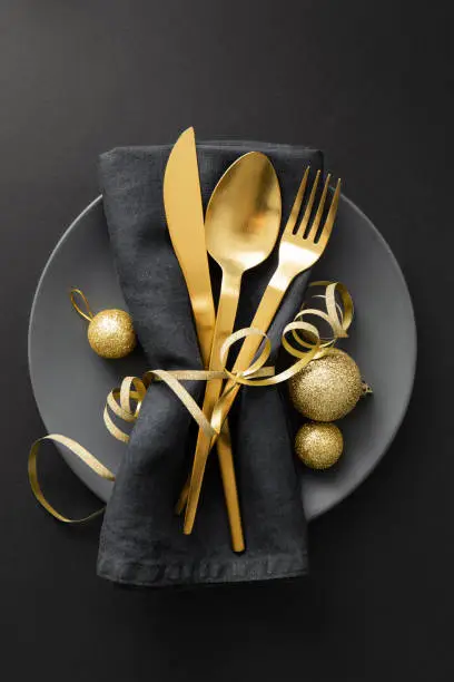 Christmas Flat Lay Background. Gold Cutlery with Bubbles served on napkin on plate on Dark Background. Minimalistic design. Copy Space. Vertical. Christmas concept.