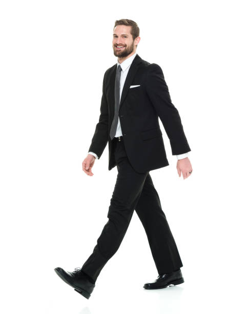 full length / one man only / side view / profile view of 20-29 years old adult handsome people / tall person brown hair / short hair caucasian male / young men business person / businessman / manager walking in front of white background - arms at side imagens e fotografias de stock