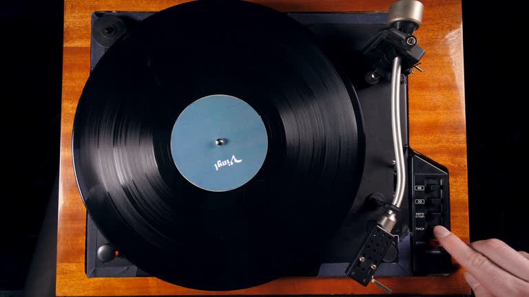 Person turns on a musical player, placing a needle on a vinyl record.