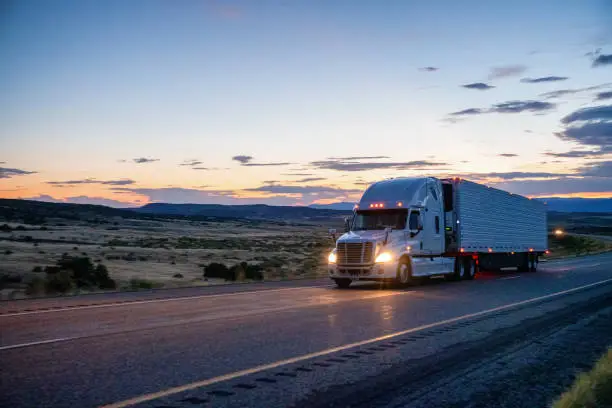 Semi-Truck Speeding down a four-lane highway with a dramatic sunset in the background and headlights on