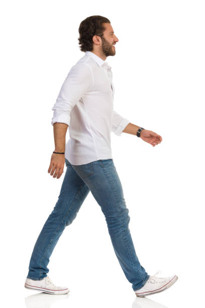 istock Smiling Man In White Shirt, Jeans And Sneakers Is Walking And Looking Away. Side View. 1173999727