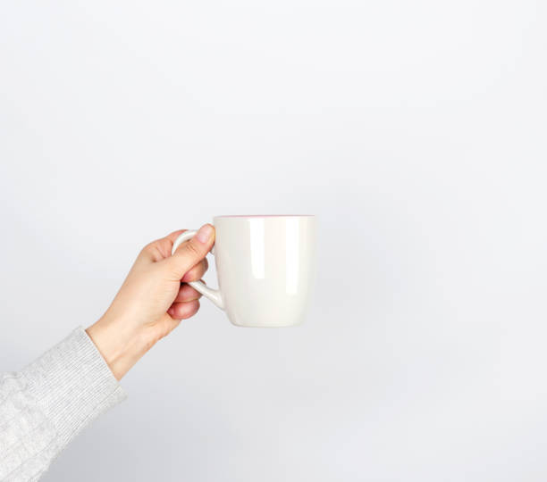 gray ceramic cup in female hand on a white background gray ceramic cup in female hand on a white background, hand raised up cup of tea hands stock pictures, royalty-free photos & images